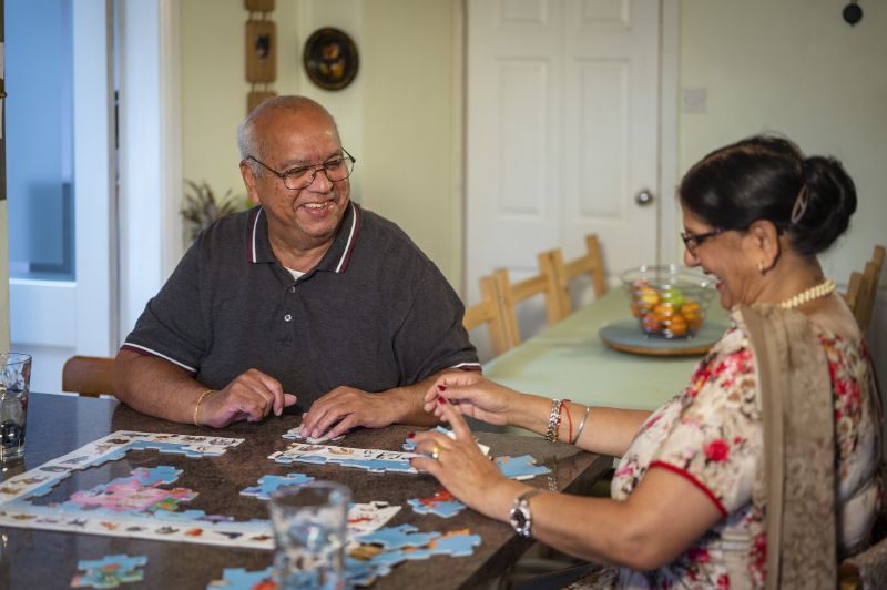 Man and Woman sat in a dining room, at a table doing a jigsaw puzzle