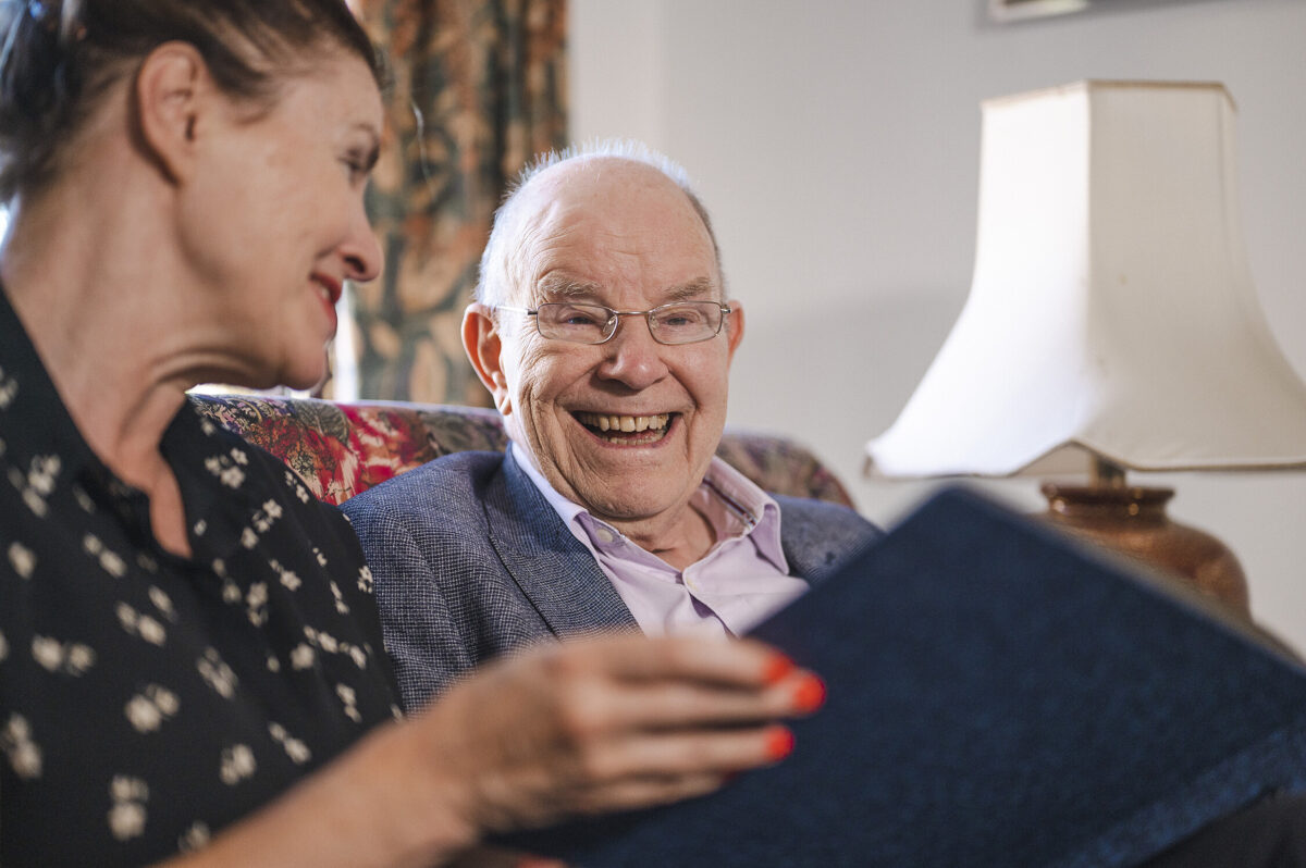 Man and woman sat on a sofa looking happily through a photo album